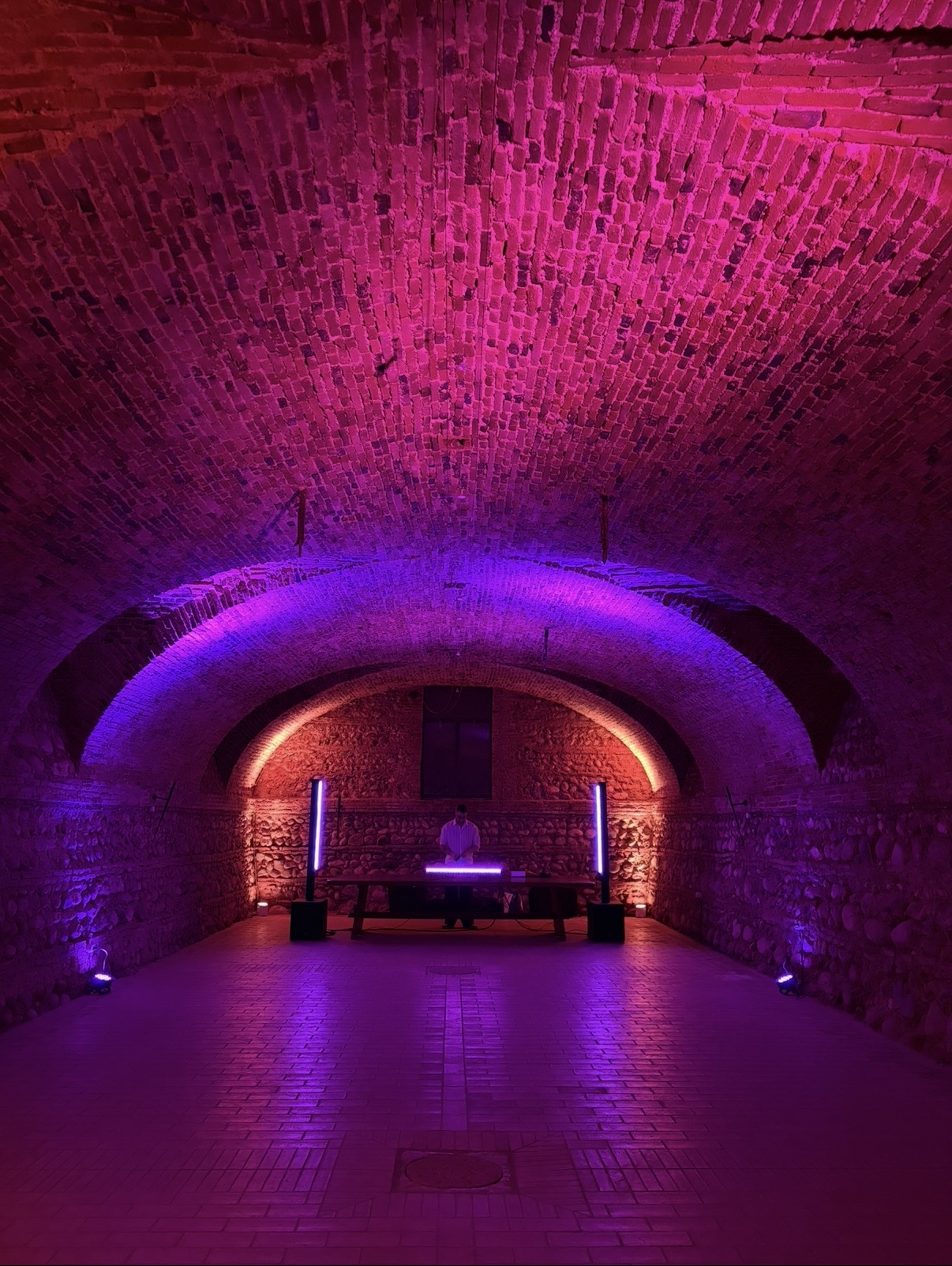 Dennis’ DJ-Aufbau unter einem Backsteingewölbe mit violettem und bernsteinfarbenem Licht